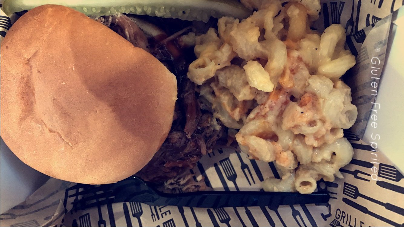 A picture of a BBQ sandwich, mac & cheese, and a pickle.