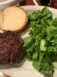 A picture of a hamburger on a gluten-free bun with a bed of lettuce on the side.